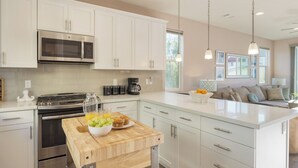 A modern kitchen with white cabinets, stainless steel appliances, and a wooden island with a bowl of fruit. - Casa do Sol by AvantStay | Rooftop Deck w/ Ocean Views | 2 blocks to Beach! (Pismo Beach)