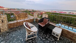 Un balcone con due poltrone in vimini e un tavolo, affacciato su un panorama urbano con edifici e un fiume.