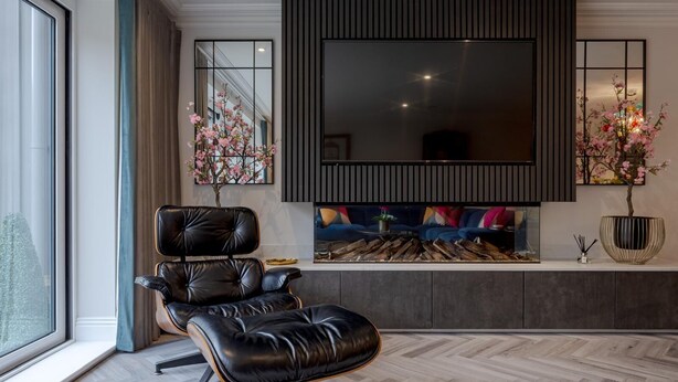 A modern living room with a black leather chair, a large flat-screen TV mounted on the wall, a fireplace with a colorful sofa, and a large window with a view of the city. - Luxury Apartment in 18th century listed Hotel conversion (Farnham)