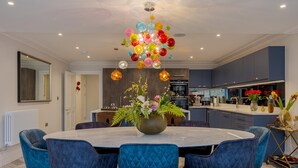 A modern dining area with a round table, blue upholstered chairs, and a decorative chandelier. - Luxury Apartment in 18th century listed Hotel conversion (Farnham)