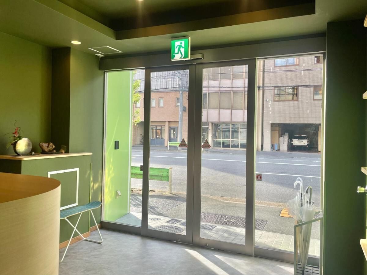 A hotel lobby with a green wall, a reception desk, and a large glass door leading outside.