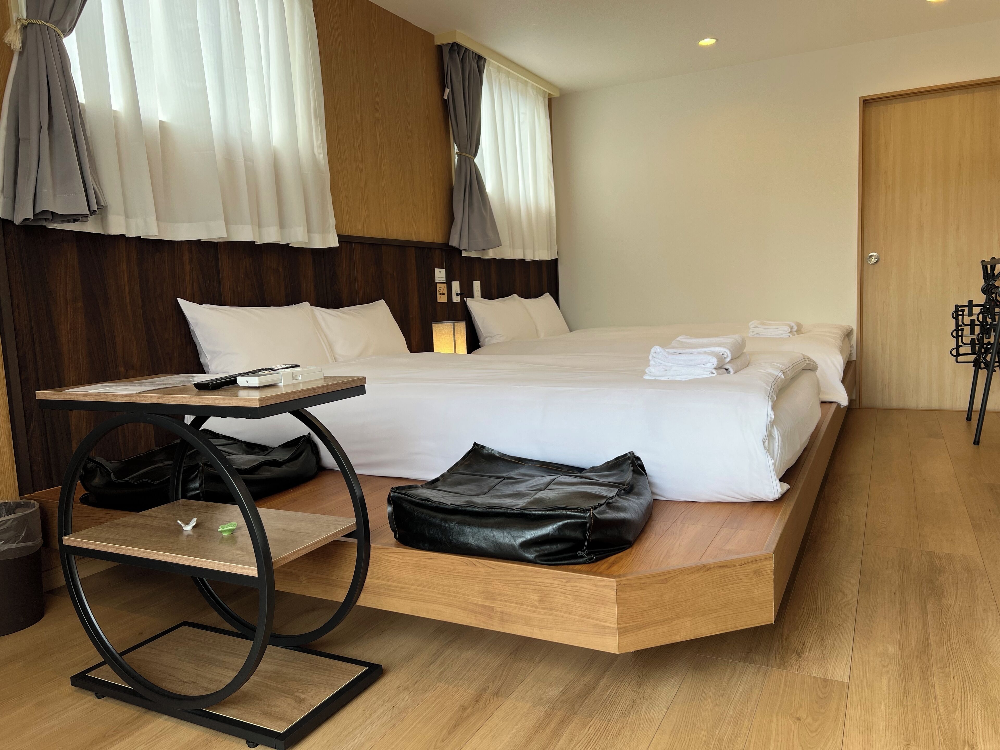A modern hotel room with a large bed, a wooden bedside table, a small desk, and a black leather bag on the bed.