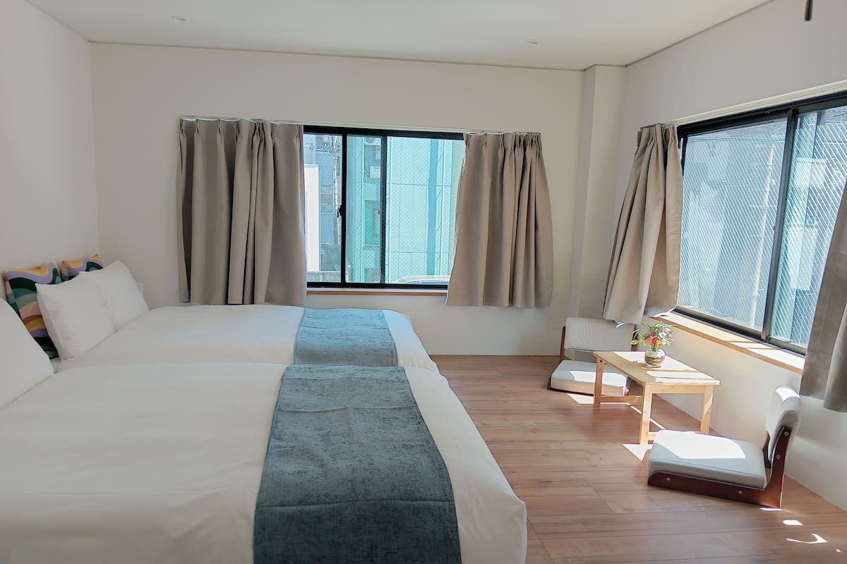 Une chambre d’hôtel moderne avec un grand lit, une petite table ornée d’un vase et une vue sur la ville grâce à de grandes fenêtres.
