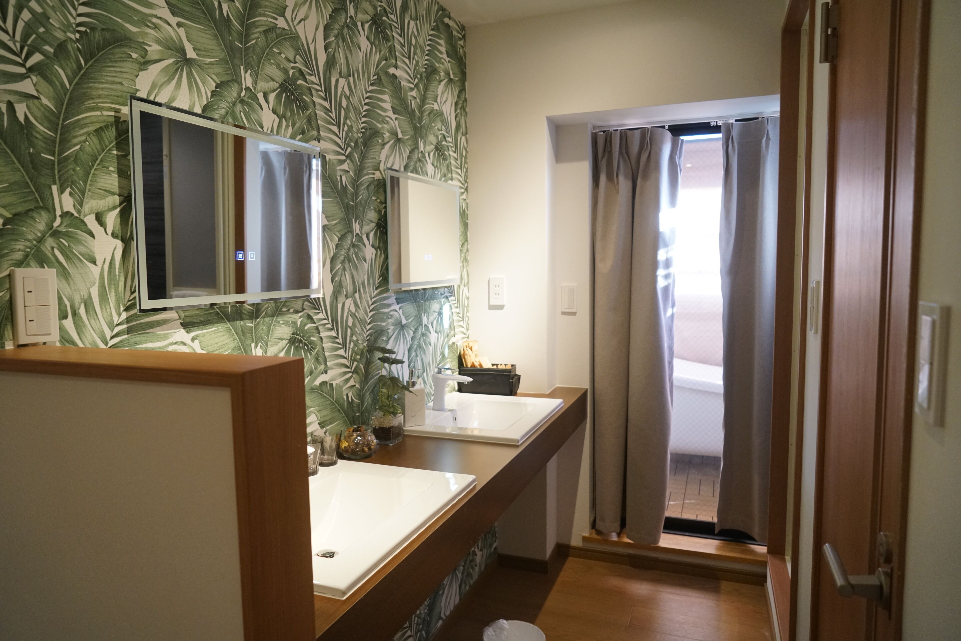 A bathroom with a large mirror, two sinks, a potted plant, and a shower area with curtains.