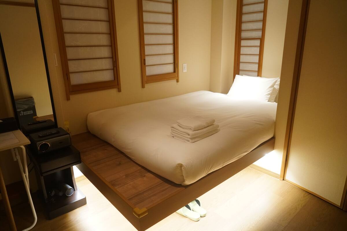 Un lit bien fait, avec une couette blanche et des oreillers, une table de chevet avec une lampe et un plancher en bois.