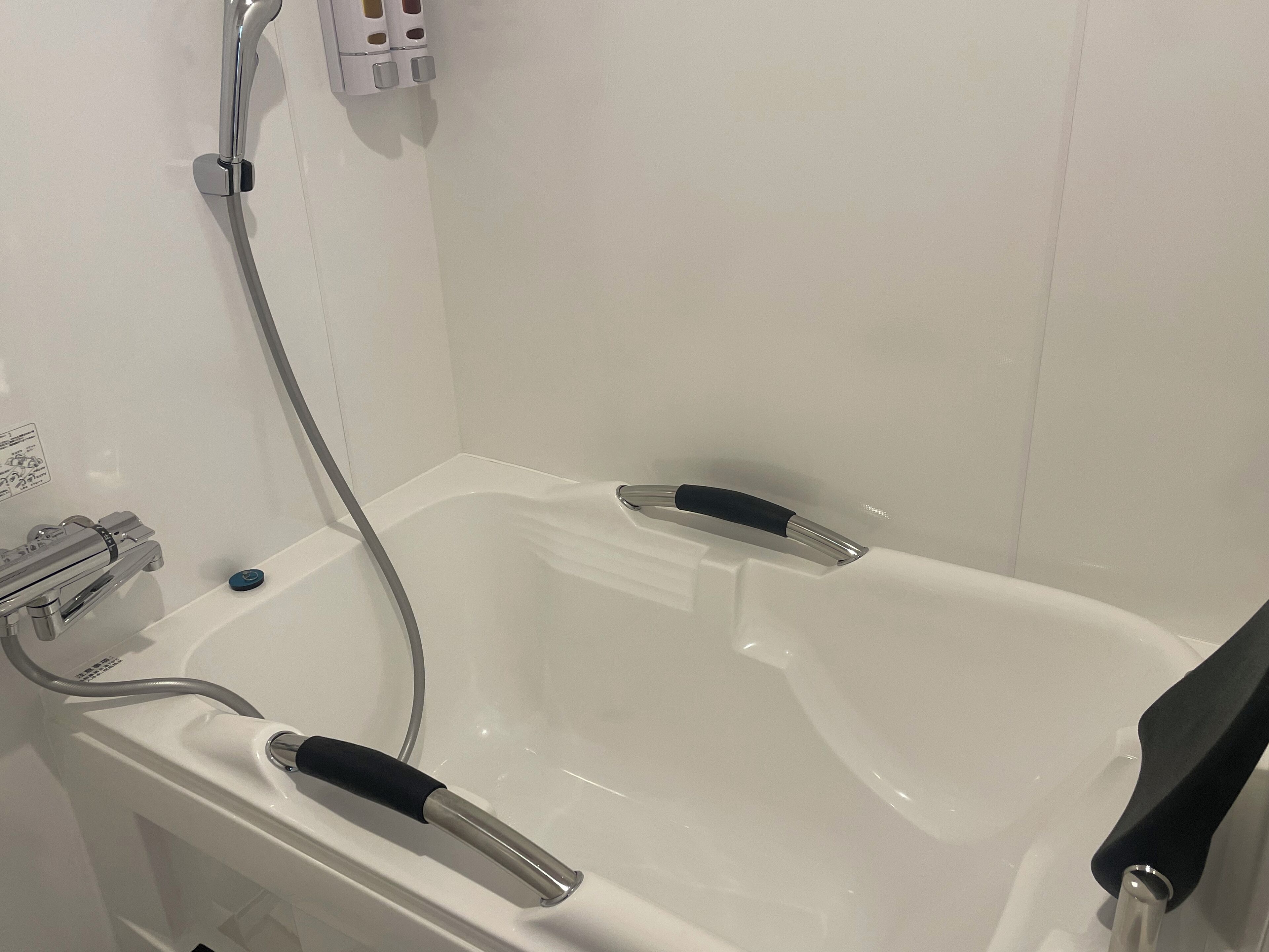Una bañera blanca con dos manijas negras, un grifo de cromo y un panel de control con un botón azul.