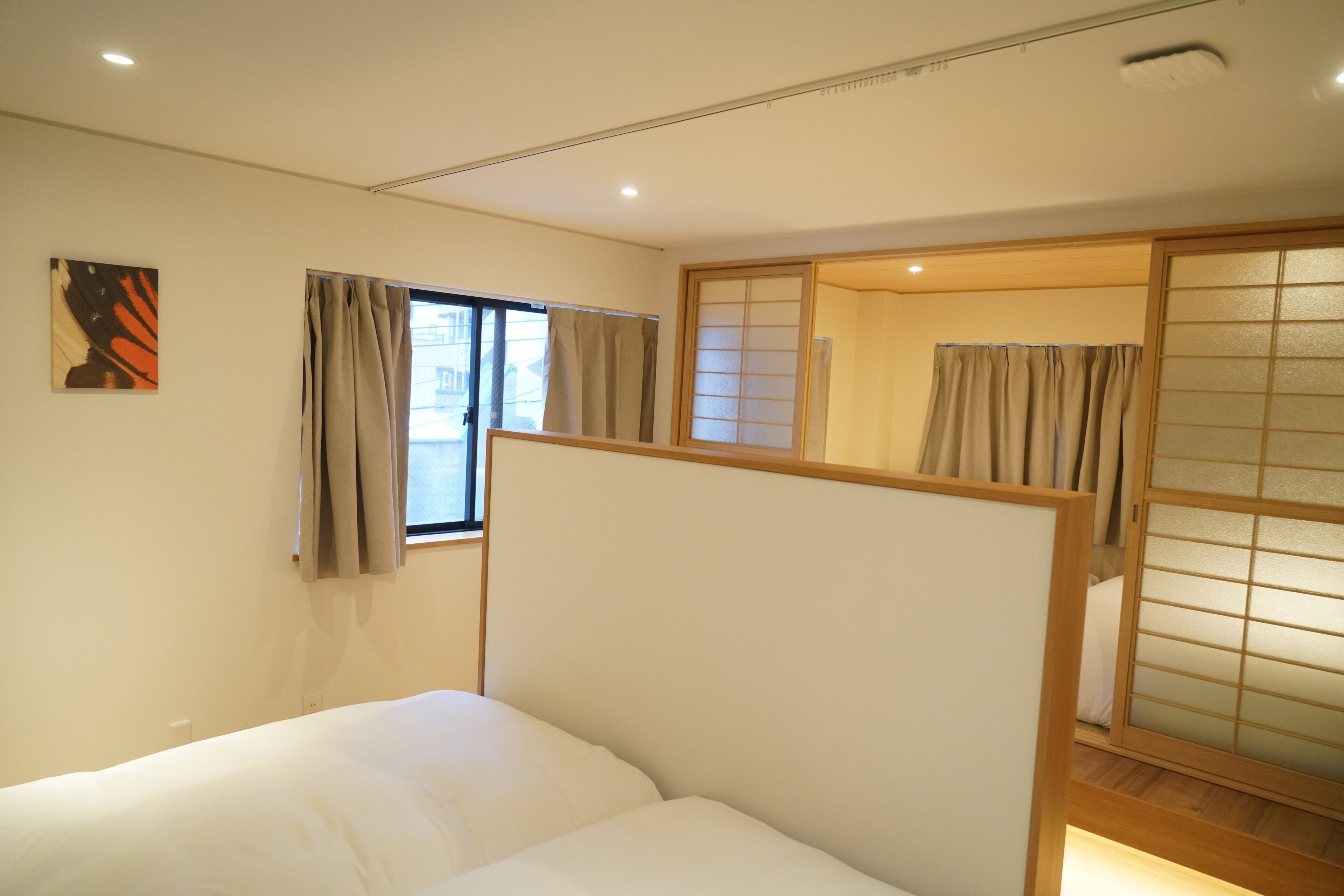 Habitación de hotel con una cama, ventana con cortinas, una obra de arte colgada en la pared y un panel corredero shoji.