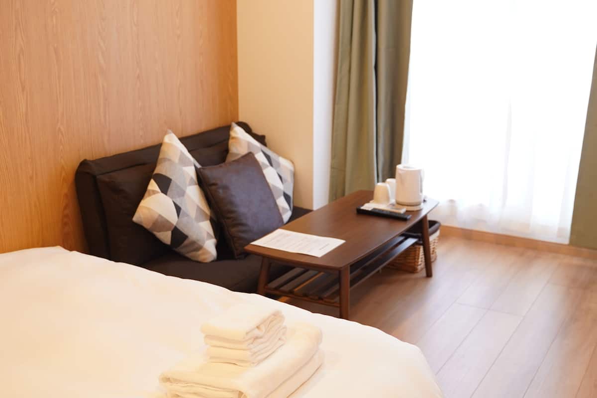 Une chambre d’hôtel avec un lit, une tête de lit en bois, une petite table avec un menu et une fenêtre avec des rideaux.