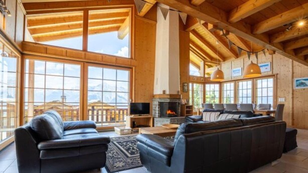A spacious living room with a fireplace, large windows, and a view of the mountains. - Sunny chalet in Veysonnaz with garden (Veysonnaz)