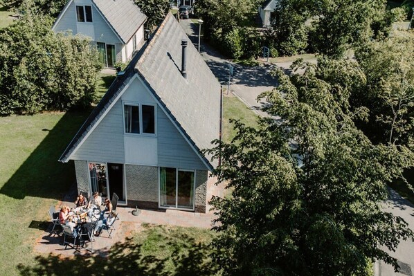 A two-story house with a sloped roof, a front porch with a dining area, and a driveway leading to a garage.