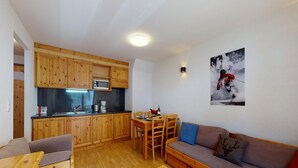 Ein kompakter Wohnbereich mit Küchenzeile, Holzmöbeln und Wandbildern zum Skifahren.