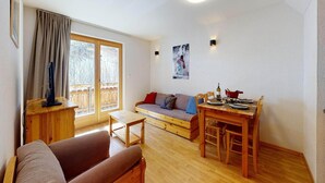 Ein gemütliches Wohnzimmer mit einer Couch, einem Esstisch für zwei Personen und einem Fernseher auf einem Holzgestell.