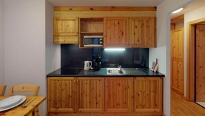A compact kitchen with wooden cabinets, a microwave, a kettle, and a sink. - Spacious apartment with view (Haute-Nendaz)