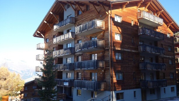 A multi-story wooden building with balconies, likely a hotel, with a mountainous backdrop. - Apartment near Piste de Tracouet (Haute-Nendaz)