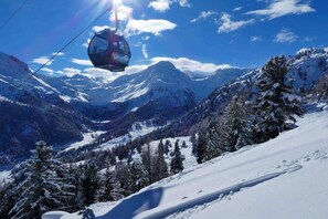 Une télécabine se déplace au-dessus d’un paysage montagneux enneigé, sous un ciel dégagé.
