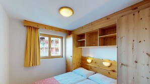 A bedroom with a wooden headboard, a window with yellow curtains, and a bed with pink and white bedding. - Apartment in Nendaz near Ski Lift (Haute-Nendaz)