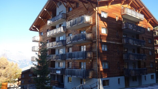 A multi-story wooden building with balconies, likely a hotel or apartment complex, with a view of mountains in the background. - Apartment in Nendaz near Ski Lift (Haute-Nendaz)