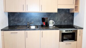 A kitchen with light wooden cabinets, a black countertop, a stainless steel sink, a coffee maker, and an oven. - Apartment in Nendaz by Ski Slopes (Haute-Nendaz)