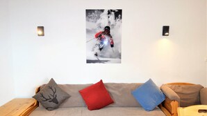 A cozy room with a sofa, pillows, and a wall-mounted picture of a skier. - Apartment in Nendaz by Ski Slopes (Haute-Nendaz)