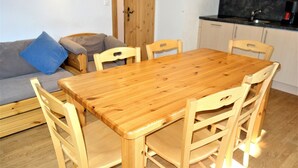A wooden dining table with six chairs, a grey sofa with a blue pillow, and a kitchen area with a black countertop and cabinets. - Apartment in Nendaz by Ski Slopes (Haute-Nendaz)