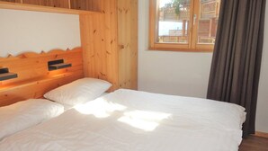 A bedroom with a wooden headboard, two white beds, a window with a view, and a curtain. - Welcoming apartment near ski area (Haute-Nendaz)