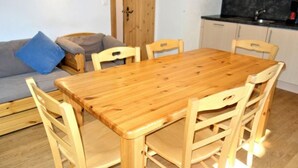 A wooden dining table with six chairs, a grey sofa with a blue pillow, and a kitchen area with a black countertop and cabinets. - Welcoming apartment near ski area (Haute-Nendaz)