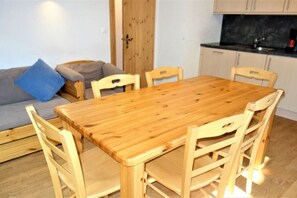 Ein Holzesstisch mit sechs Stühlen, ein graues Sofa mit einem blauen Kissen und ein Küchenbereich mit schwarzer Arbeitsplatte und Schränken.