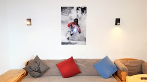 A cozy room with a sofa, pillows, and a wall-mounted picture of a skier. - Welcoming apartment near ski area (Haute-Nendaz)