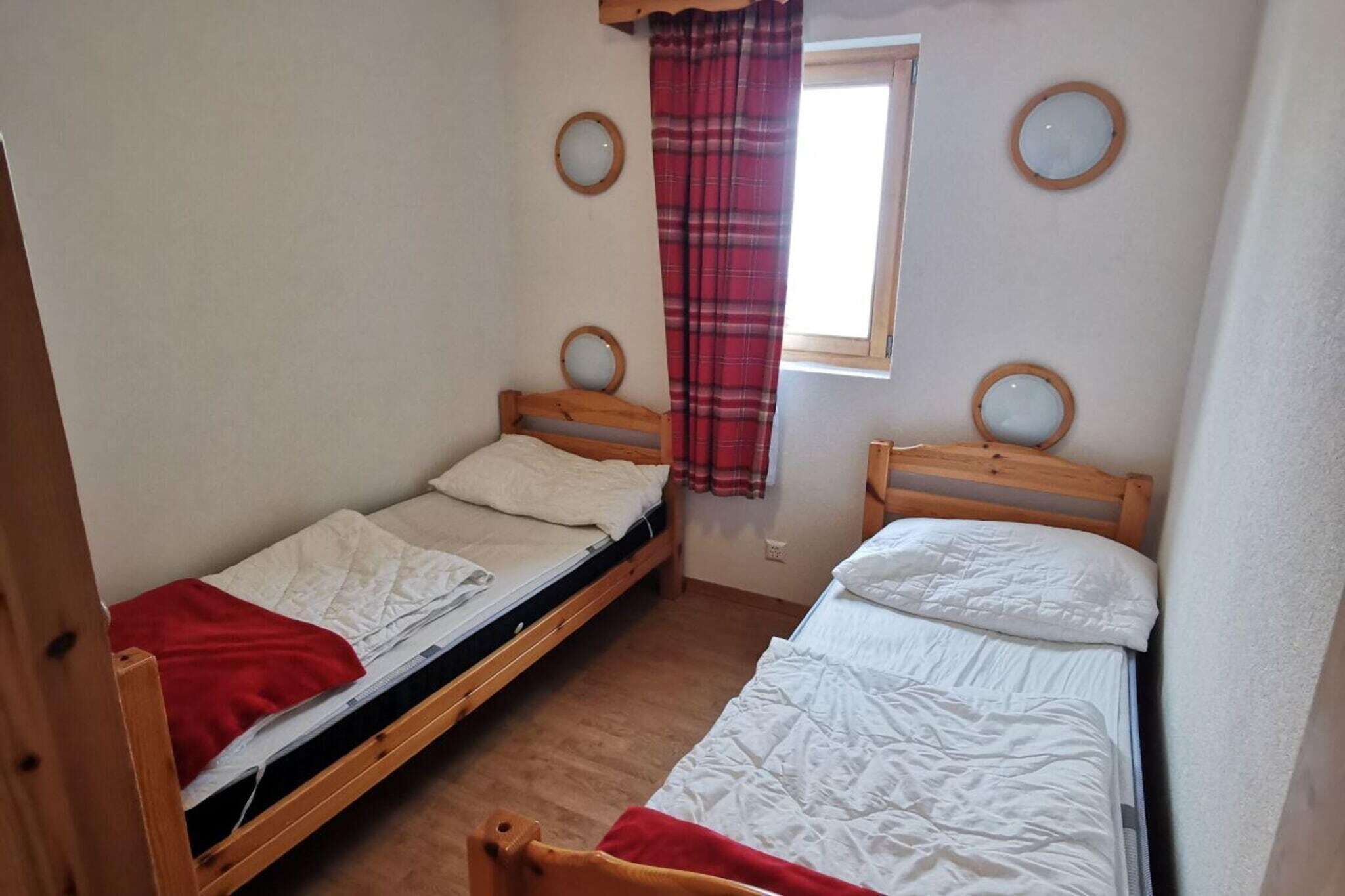 Una habitación pequeña con dos literas de madera, una ventana con cortina roja y espejos redondos colgados en la pared.
