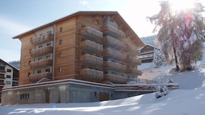 A multi-story wooden building with balconies, surrounded by snow. - Valley-view apartment with balcony (Haute-Nendaz)