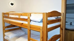 A bunk bed with white bedding, a wall-mounted light fixture, and a bathroom with a sink and cabinet. - Valley-view apartment with balcony (Haute-Nendaz)
