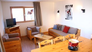 Una habitación acogedora con una mesa de madera, un sofá, un televisor y una ventana con cortinas.