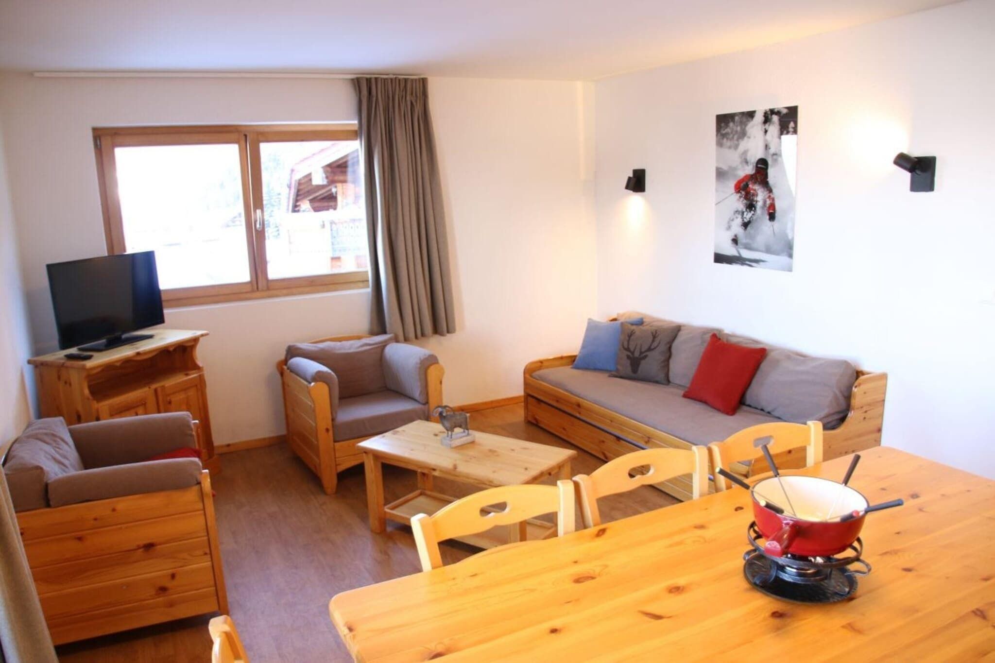 Een knus ingerichte kamer met een houten bank, een klein tafeltje, een televisie en een raam met gordijnen.