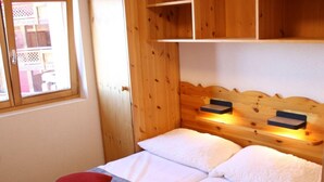 Una cama doble con ropa blanca y almohada roja, cabecera de madera y estantes empotrados sobre la cama.