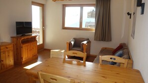 A wooden dining table with chairs, a television on a wooden cabinet, a window with curtains, and a sofa. - Charming apartment with balcony (Haute-Nendaz)