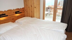 A double bed with white linens in a room with wooden paneling and a view of outdoor furniture through a glass door. - Charming apartment with balcony (Haute-Nendaz)