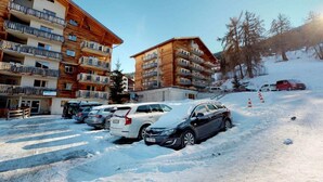A multi-story hotel with balconies and a parking area covered in snow. - Charming apartment with balcony (Haute-Nendaz)