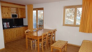 A compact room with a wooden dining table, chairs, a small kitchen with a microwave, and a bed with a floral bedspread. - Nice apartment next to cable car (Haute-Nendaz)