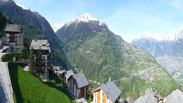 A mountain village with chalet-style buildings, a winding road, and a snow-capped mountain in the background. - Nice apartment next to cable car (Haute-Nendaz)