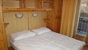 A wooden room with a bed, two wall-mounted shelves, and a window with a view of a wooden deck. - Nice apartment next to cable car (Haute-Nendaz)