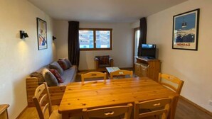 A cozy living room with a wooden dining table, a sofa, and a television. - Nice apartment next to cable car (Haute-Nendaz)