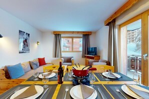 A dining area with a table set for four, a bottle of wine, and a red pot on the table. - Attractive apartment for family (Haute-Nendaz)