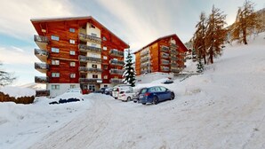 Et hotel med flere etager, altaner, en skibakke og parkerede biler.