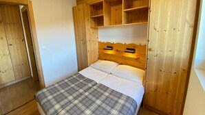 Un dormitorio con cabecera de madera, cama con ropa de cama blanca y manta a cuadros.