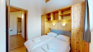 A bedroom with a wooden headboard, a bed with white linens, and built-in shelving above the bed. - Spacious apartment with balcony (Haute-Nendaz)
