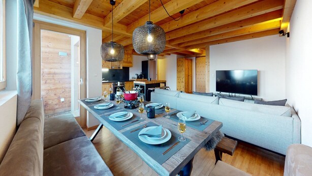A modern living room with a wooden ceiling, a dining table set for four, and a large flat-screen TV on the wall. - Spacious apartment with balcony (Haute-Nendaz)