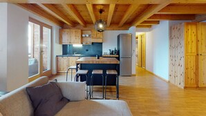 A modern kitchen with wooden beams, a central island, bar stools, and a refrigerator. - Spacious apartment with balcony (Haute-Nendaz)