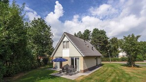 A single-story house with a sloped roof, a patio with a table and chairs, and a blue umbrella.