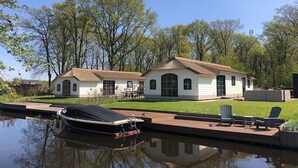 Una casa con muelle y bote, rodeada de árboles y césped.