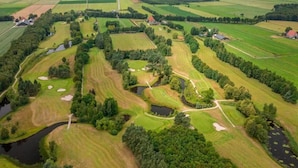 Vista aérea de un campo de golf con múltiples áreas verdes, obstáculos acuáticos y algunos edificios.